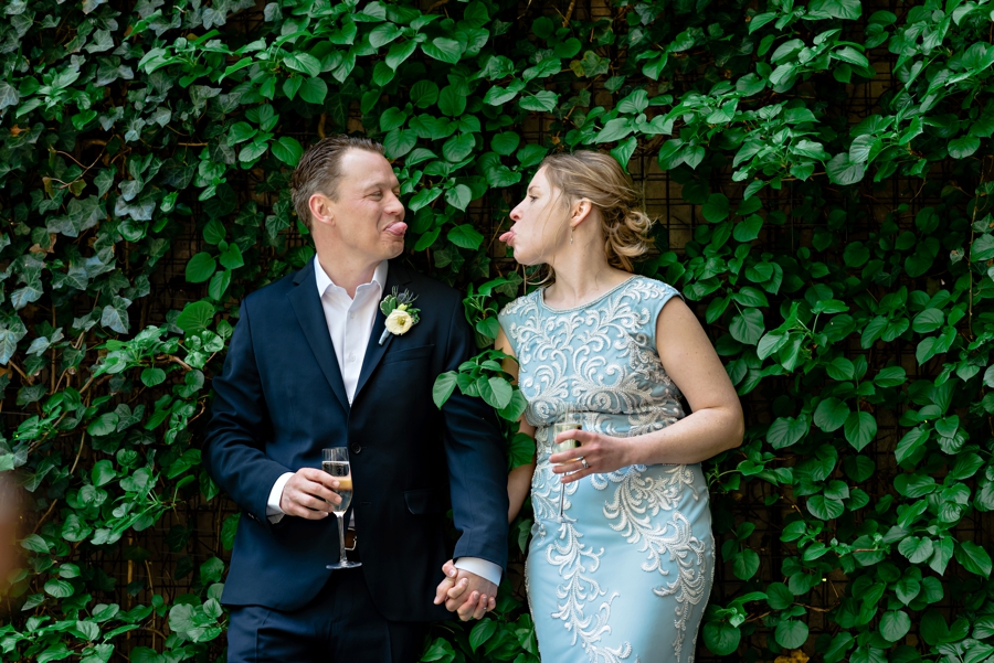 A fun couple acts silly in front of an ivy wall.
